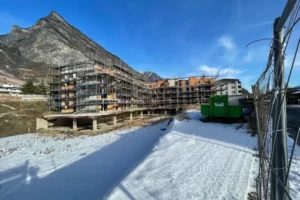 chantier de construction à Leytron avec un bâtiment en échafaudage, situé au pied d'une montagne, sous un ciel bleu clair avec de la neige au sol.